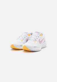 Scarpe da ginnastica bianche con accenti rosa, suole gialle e una texture in rete. Presentano una chiusura con lacci e punte perforate per una migliore traspirazione.