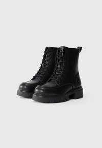 Black leather ankle boots with a rounded toe, flat treaded sole, lace-up front, and a pull tab at the back for easy wearing.