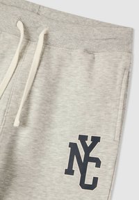 Szare dresy wykonane z miękkiego materiału z prążkowanym paskiem w talii. Posiadają niebieskie logo "NYC" na lewej nogawce. Zawierają sznurki do regulacji.