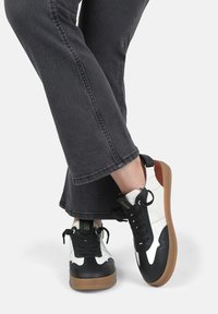 Sneaker bianco e nero con suola in gomma presentano un mix di materiali, tra cui pelle e tessuto, e lacci con dettagli a occhiello.