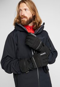 Schwarze isolierte Handschuhe mit geripptem Design und weißen Akzenten. Hergestellt aus strukturiertem Material, mit verstellbaren Riemen für einen sicheren Sitz.