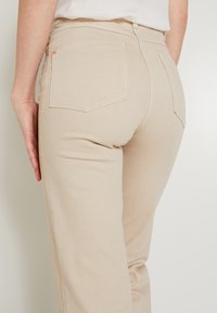 Jeans de mezclilla beige con un diseño ajustado, que cuentan con dos bolsillos traseros, costuras limpias y una textura sutil. Sin desgastes visibles.