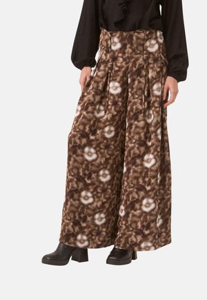 Pantalones anchos marrones con estampado y pliegues, combinados con un top negro de manga larga y botines negros con tacón.