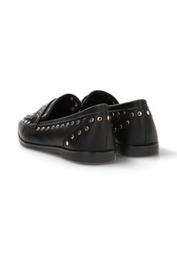 Zapatos de cuero negro con una textura suave, que presentan detalles metálicos en los ojales a lo largo de los costados y una suela plana de goma.