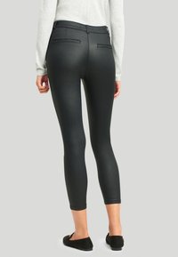 Svarta leggings i faux läder med smal passform, midja i mellanhöjd och två bakfickor, tillsammans med en ljusgrå tröja och svarta lägenheter.