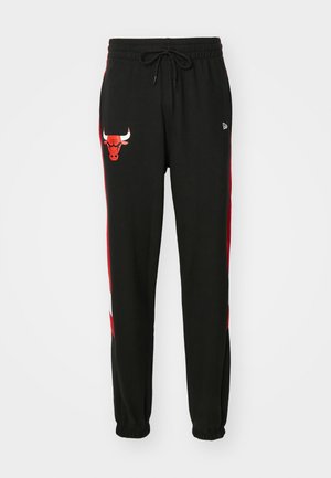 Pantalon de survêtement noir avec des rayures latérales rouges, taille élastique, cordon de serrage et un graphisme d'une tête de taureau sur la cuisse gauche.