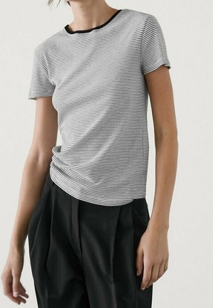 Person wearing a short-sleeve, black and white striped t-shirt with a black collar paired with high-waisted black pants.