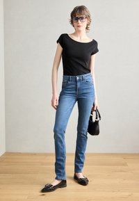 Top negru cu mânecă scurtă, blugi albaștri cu talie înaltă și pantofi negri. Accesoriile includ o geantă mică neagră și ochelari albaștri. Podea din lemn deschis.