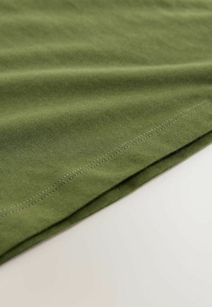 Groen katoenen stof met een gladde textuur, voorzien van een omgevouwen zoom en subtiele stikseldetails langs de rand.