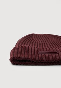 Złożona czapka dzianinowa o prążkowanej strukturze w ciemnym burgundzie z prostokątną naszywką logo Tommy Hilfiger na mankiecie, widoczną z przodu.
