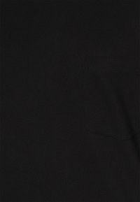 Tela negra con una textura suave, que presenta un pequeño bolsillo con un borde cosido simple. El material parece duradero y ligero.