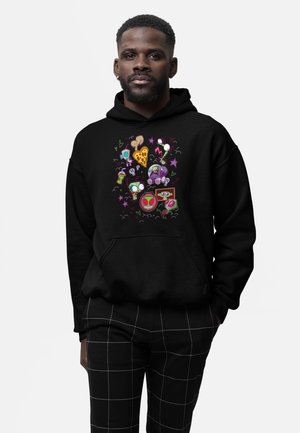 Man draagt een zwarte hoodie met kleurrijke cartoonfiguren en voedselitems, gecombineerd met zwarte broek met witte rasterslijnen.
