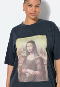 Černé oversized tričko s vybledlým potiskem Mona Lisy, krátké rukávy a kulatý výstřih. Měkká bavlněná textura.