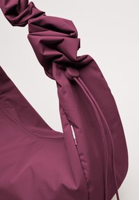 Bolso burdeos con una correa texturizada y fruncida y un detalle de cremallera, hecho de tela suave. Diseño compacto con elegantes acentos de costura.