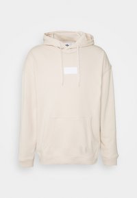 Beige huppari kengurun taskulla, kiristysnauhalla varustetulla hupulla ja suorakaiteenmuotoisella valkoisella logolla rinnassa. Pehmeä kangas ja rento istuvuus.