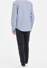 Vaaleansininen ruudullinen paita, jossa on pitkät hihat ja nappimansetit, yhdistettyinä tummansinisiin housuihin ja valkoisiin lenkkareihin.