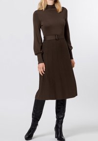 Hnědressovaný žebrovaný pletený šaty s vysokým výstřihem, dlouhými rukávy a pasem s opaskem. Dark vysoké boty ke kolenům dokončují look.