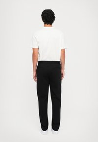 Mannenoutfit met een wit T-shirt met korte mouwen en zwarte broeken met een ontspannen pasvorm, elastische tailleband en zijzakken. Witte sneakers.