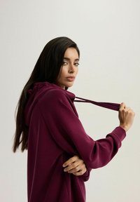 Burgundowa bluza z kapturem, wykonana z miękkiego materiału. Charakteryzuje się luźnym krojem i marszczeniem na kapturze.