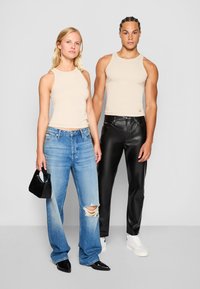 Bež majice brez rokavov, uničeni svetlo modri jeans in črne hlače iz umetnega usnja. Dodatki vključujejo majhno črno torbico in bele superge.