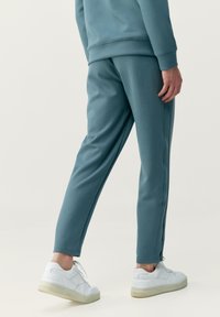 Svetlomodré teplákové nohavice so zúženým strihom, elastickým pásom a viditeľnými švami. V kombinácii s bielymi teniskami s textúrovanou podrážkou.