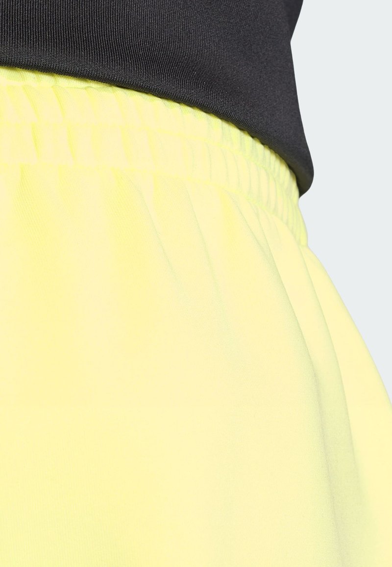Black top tucked into bright yellow elastic-waist pants, showing fabric texture and waist detail against light background.