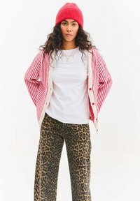Pruhovaný červeno-bílý kardigan přes bílé tričko, doplněný širokými kalhotami s leopardím vzorem. Součástí jsou knoflíky a červená čepice s texturou.
