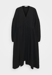 Svart långärmad klänning med V-ringning, rynkad midja och flytande silhuett. Tillverkad av lätt, strukturerad tyg.
