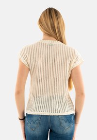 Gebreid kortmouwtopje, lichtbeige met opengebreid patroon, ronde halslijn en zachte textuur, gecombineerd met denim jeans.