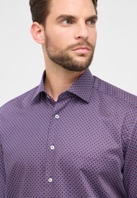 Langsleeve shirt in diep paars met een geometrisch patroon. Voorzien van een klassiek kraag en witte knopen. Gladde stoffen textuur.