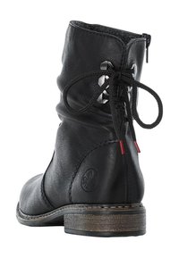 Zwarte leren enkellaars met een zachte bovenkant, decoratieve veters, metalen accenten en een lage, gestructureerde hak. Ritsluiting aan de zijkant.