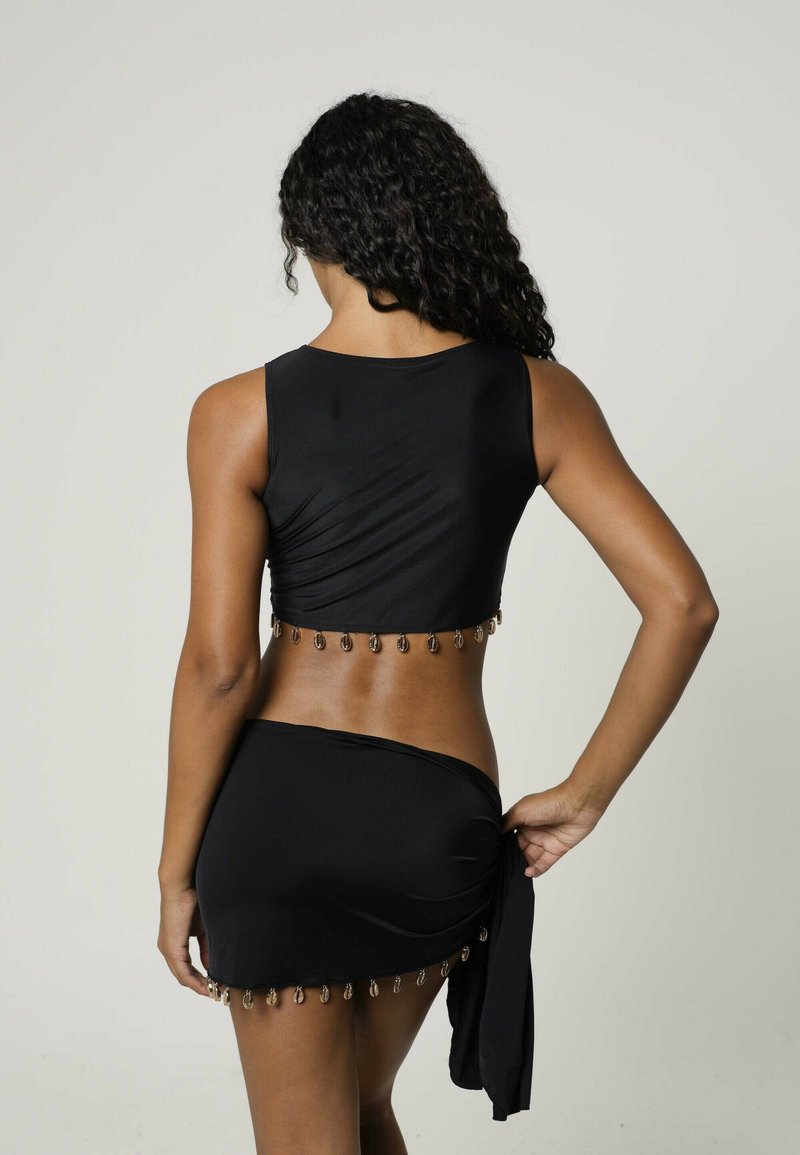 Schwarzes Zweiteiler-Outfit mit einem cropped Top in gerafftem Design und einem Minirock, der am Saum mit metallischen Akzenten verziert ist.