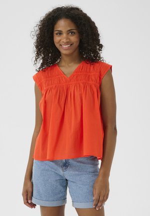 Lys orange ærmeløs bluse med V-hals og rynket detaljering foran, parret med blå denimshorts. Enkel og afslappet pasform.
