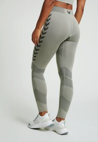 Högmidjade leggings i ljusgrått med texturerade paneler och svarta zigzag-mönster längs sidorna; matchas med vita träningsskor.