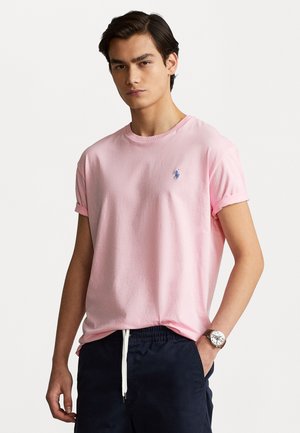 Ljusrosa bomullst-shirt med upprullade ärmar, med en liten blå logo på bröstet, kombinerad med marinblå elastiska shorts.