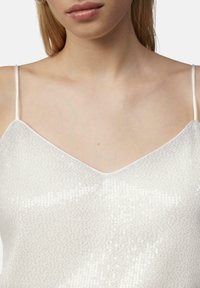 Silberne Pailletten-Bluse mit verstellbaren dünnen Trägern und V-Ausschnitt, die eine glatte Textur und metallischen Glanz auf einem hellen Hintergrund aufweist.