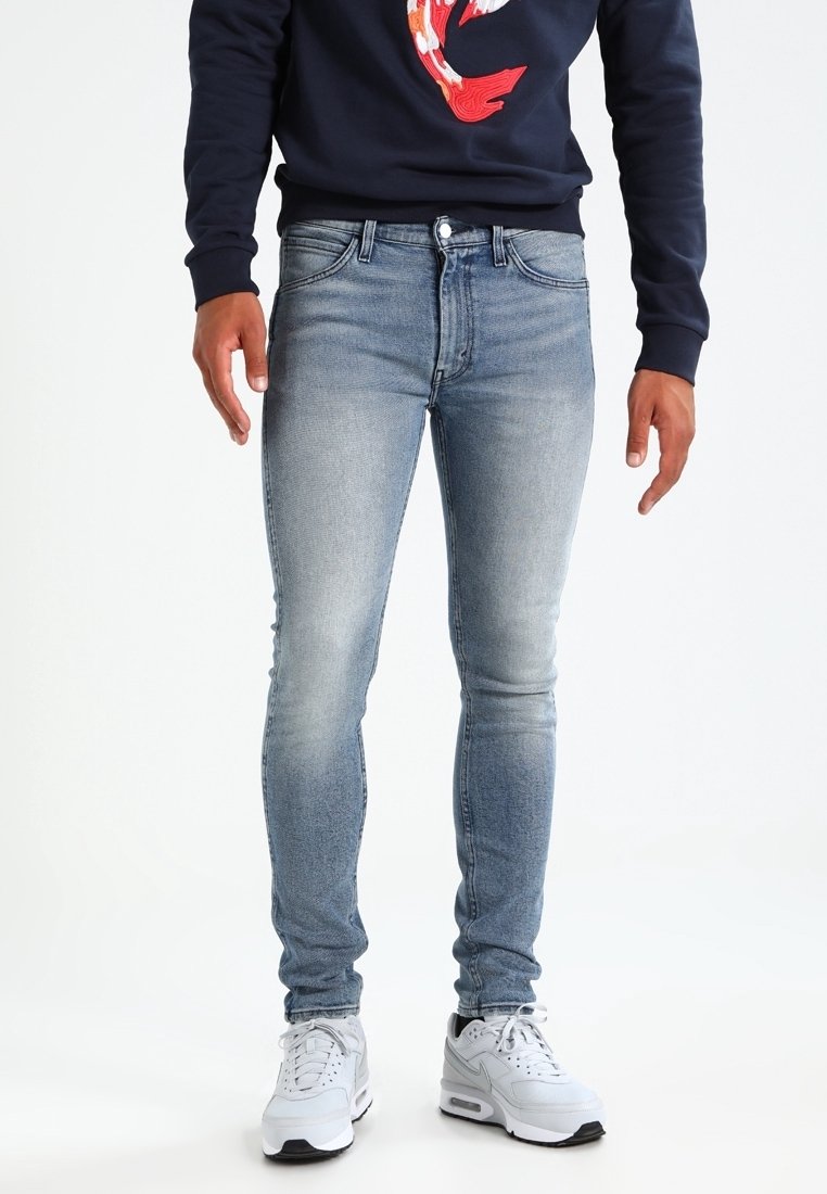 Světle modré džíny skinny se sepraným vzhledem, pěti kapsami a zapínáním na knoflík, doplněné bílými sportovními teniskami.