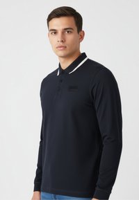 Marineblaues Langarm-Poloshirt aus strukturiertem Stoff, mit einem weißen Kragenstreifen und einem dezenten Logo auf der Brust.