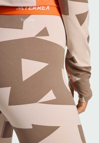 Mallas con patrones en marrón y beige claro con formas abstractas. Presentan una cinturilla naranja con la etiqueta "TERREX" y el logo "CLIMACOOL".