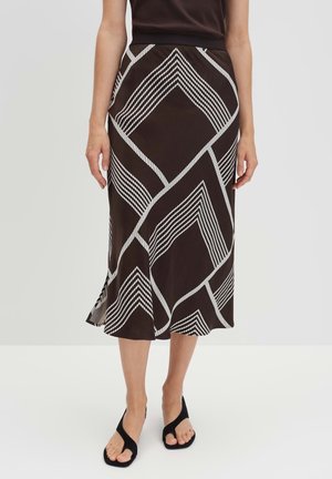 Mujer con una falda midi negra con grandes patrones geométricos de diamante en blanco y sandalias negras abiertas en la punta.