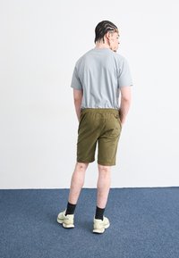 T-shirt gris, shorts vert olive avec taille élastique, poche latérale et détail à l'arrière. Comprend également des baskets légères et des chaussettes noires.