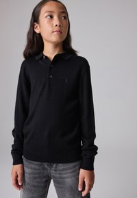 Must mustaga polo särk pika varrukaga pehmest materjalist, millel on krae ja kolm nuppu, ning rinnal on väike broderi logo.