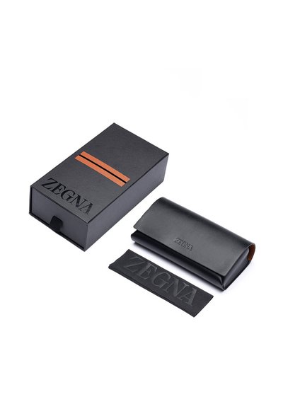 Černá kožená pouzdra na brýle s embosovaným logem, doplněná černou krabičkou s hnědým proužkem a odpovídajícím logem na přední straně.