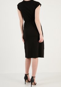Czarna, do kolan sięgająca sukienka dresowa z krótkimi rękawami i dopasowanym talią. Noszona z czarnymi sandałami na wysokim obcasie, z paskiem wokół kostki.