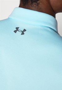Lichtblauwe polo met een textuurstof, voorzien van een zwart logo op de kraag. De kraag heeft een klassiek ontwerp en is geribbeld.