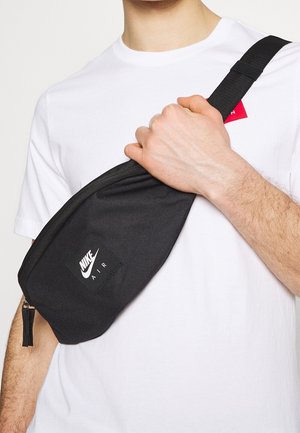 Banane noire Nike Air avec une texture lisse, une fermeture zippée et un patch logo. À porter en bandoulière, avec une sangle réglable.