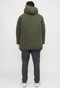 Olivenfarvet polstret jakke med hætte, der har en glat tekstur og et let forlænget design, parret med mørkegrå cargo-bukser.