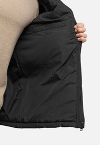 Chaqueta acolchada negra, que presenta una tela suave y brillante. El interior cuenta con un bolsillo. Cierre de cremallera en la parte delantera y un diseño acolchado.