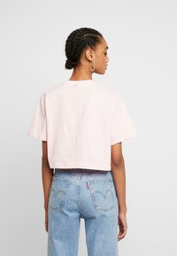 Gaiši roz�ā īsa krekla T-kreks ar īsām piedurknēm un apaļu kakla izgriezumu, apvienots ar gaiši zilām džinsām, kurām ir aizmugurējās kabatas un izbalējusi apdare.