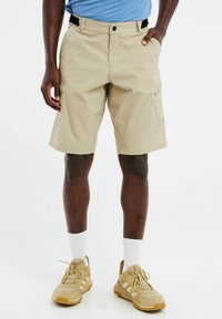 Beige cargoshorts met een casual pasvorm, voorzien van zijzakken, een gladde textuur en een verstelbare taille, gecombineerd met tan-sportschoenen en witte sokken.